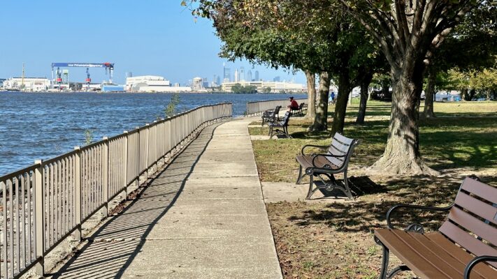 A walkway by the Delaware River in Red Bank Battlefield Park in National Park, New Jersey. The Philly Shipyard and Downtown Philadelphia can be seen in the background.